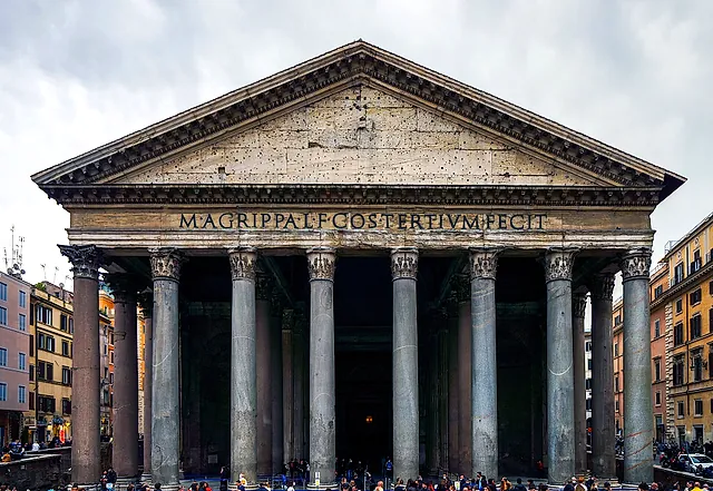 The Pantheon façade from the square: grey columns of the portico, the triangular pediment with the Agrippa inscription, and a crowd of visitors under a cloudy sky