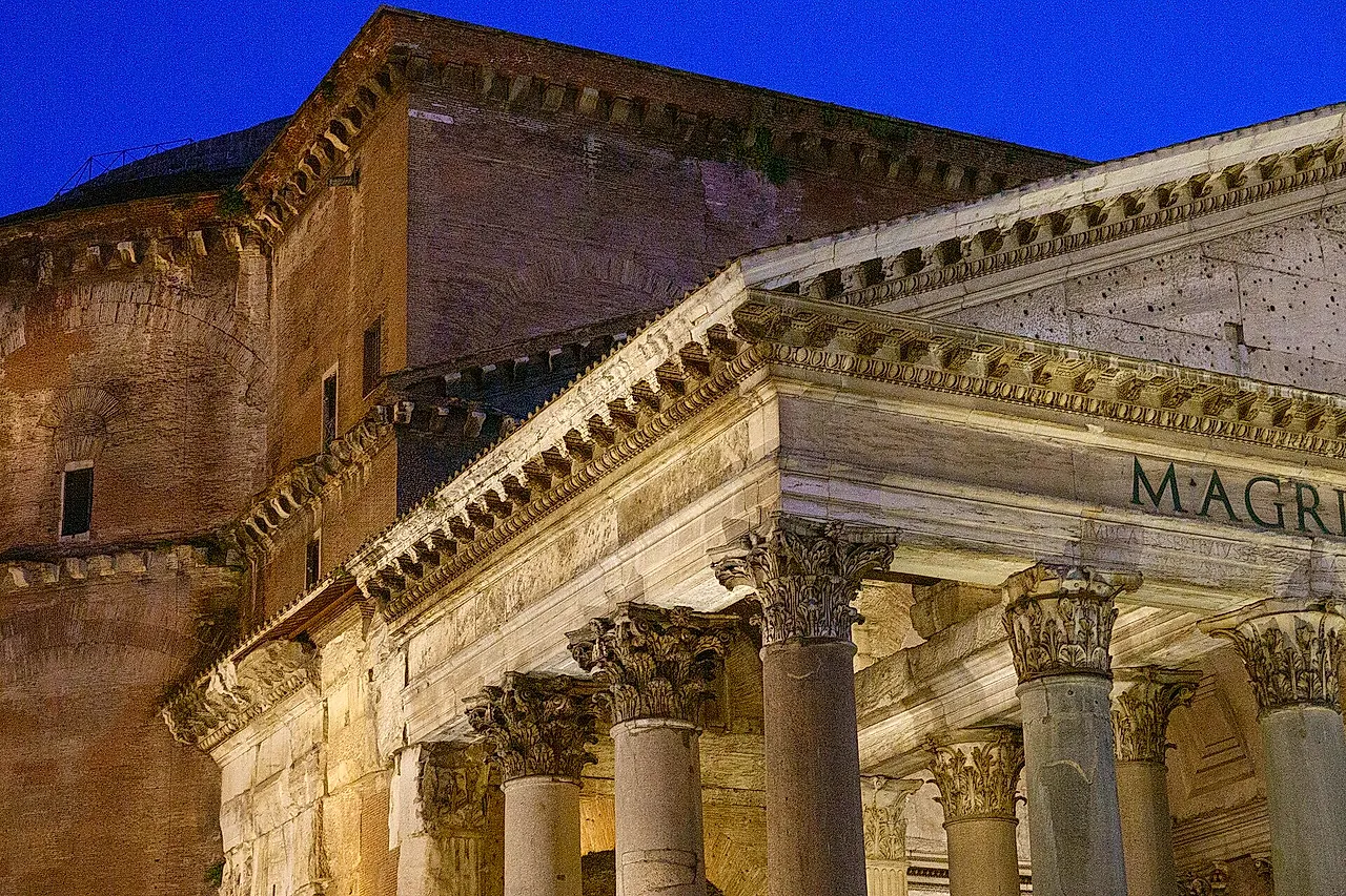 The Pantheon portico at dusk: Corinthian columns and the pediment lit from below, with the brick drum of the dome behind against a deep blue sky