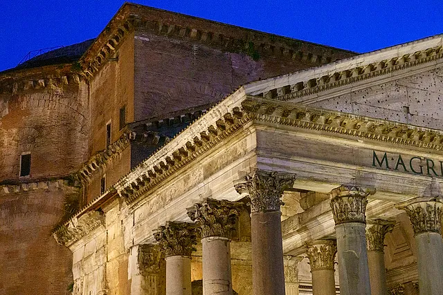 The Pantheon portico at dusk: Corinthian columns and the pediment lit from below, with the brick drum of the dome behind against a deep blue sky